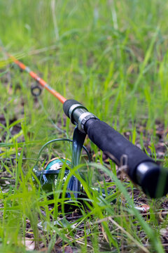 Vertical close-up of fishing rod handle and spinning reel in green grass