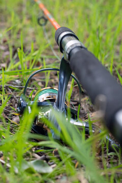 Vertical close-up of orange fishing rod reel lying in grass
