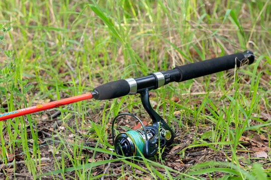 Horizontal shot of bright orange fishing rod with spinning reel on green grass