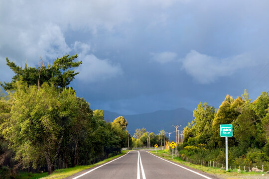 Horizontal wide shot of asphalt highway heading toward mountains under dramatic stormy sky