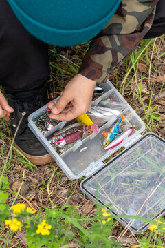 Vertical high-angle shot of angler selecting lures from a plastic tackle box