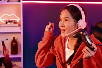 Host channel of smiling beautiful Asian girl streamer with joystick playing with raising fist up winning Esport skilled team players wearing headphones pastel media online in neon room. Stratagem. © InfiniteFlow