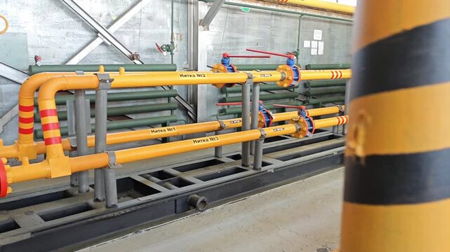 Yellow pipe assembly in plant control room with valves and gauges. Industrial system runs along steel supports while blue access doors and safety markings frame equipment, creating precise utility
