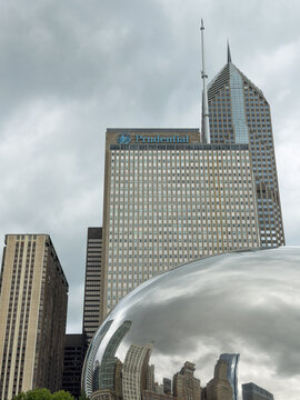 CHICAGO, IL, JUN 18, 2026: Vertical view of the Prudential building and a pointed neighboring tower rising behind Cloud Gate, which reflects the skyline under a heavy, overcast sky