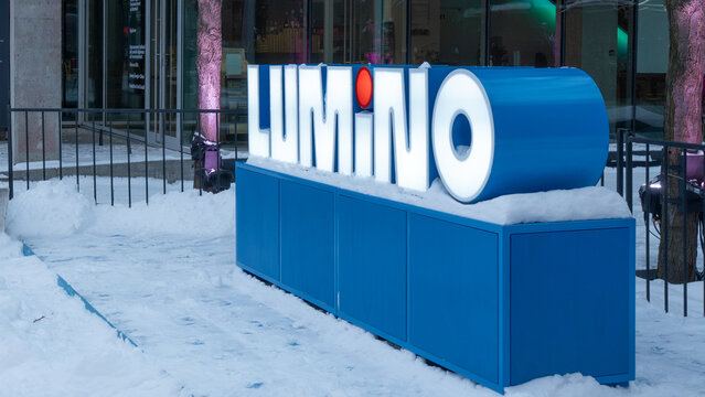 Illuminated LUMINO sign on blue outdoor display surrounded by snow and winter lights in a contemporary urban setting