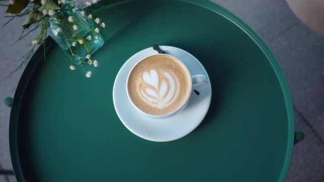 Latte art in a cafe on a green table with a small vase