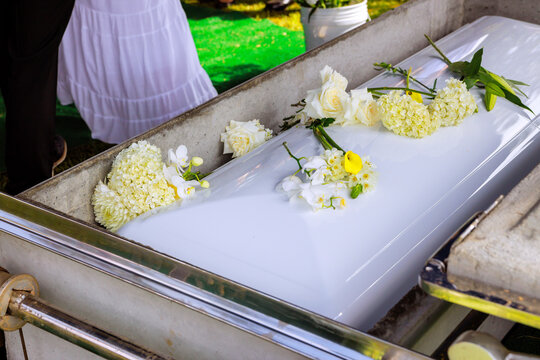 Casket with white flowers during burial ceremony at grave site