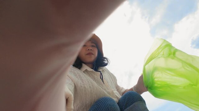 The view from the trash heap. POV: A women picks up trash against a blue sky with clouds. Wide angle shot. Fisheye. People taking care of nature. Ecology in danger. Stop the overproduction.