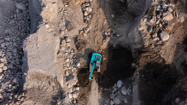 Aerial view of an excavator working in a deep dirt pit with rocky terrain and shadows cast on the ground in Indonesia