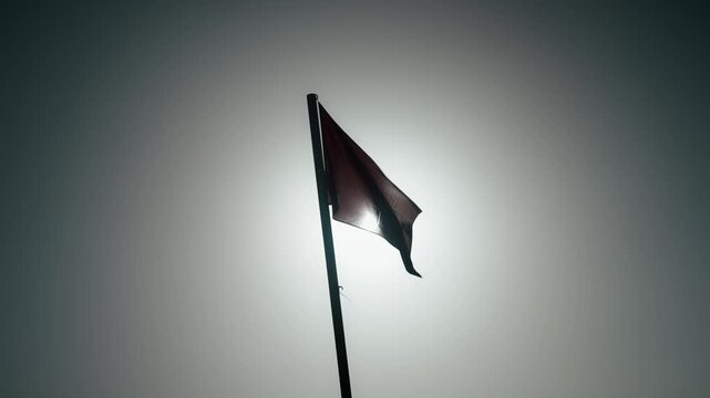 A red Moroccan flag with a green star flutters on a tall pole, with sunlight shining through its shifting folds against the sky.