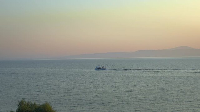 Stunning twilight coastal view of the Aegean Sea, a traditional fishing boat cruising calm waters accompanied by a large flock of seabirds, Mytilene, Lesvos, Greece.