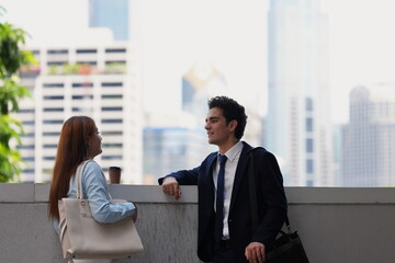 Fototapeta premium Business colleagues talking at a terrace wall with the city skyline behind them, a wide image of an outdoor break for corporate and property marketing, in soft hazy daylight