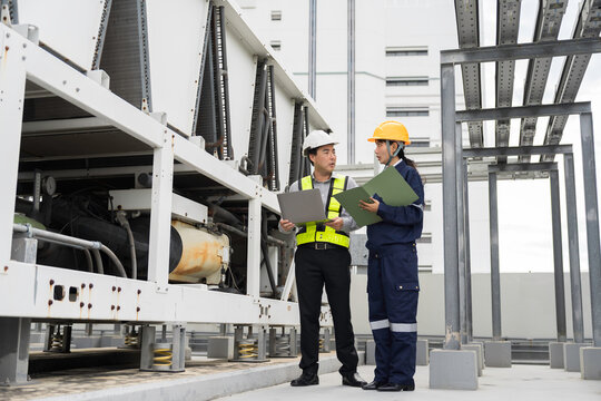 Asian engineer and technician inspecting rooftop air-cooled chiller unit during HVAC maintenance. Asian male engineer and female technician inspection spring-mounted HVAC equipment building roof