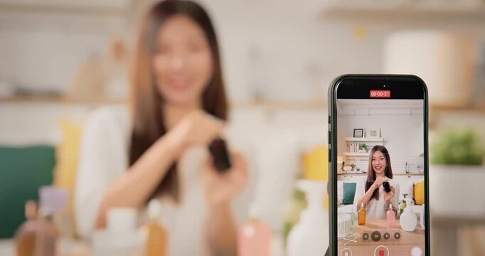 Asian woman beauty influencer, content creator filming skincare product review on smartphone at home. Gen Z lifestyle social media trends. digital marketing, promotions, cosmetic branding vlogs.