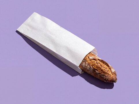 Fresh crusty baguette in white paper bag on purple background