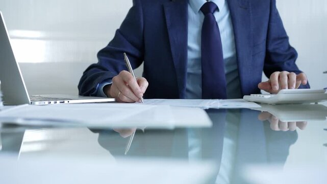 Businessman using calculator and taking notes, working with laptop and documents at office desk. Audit and taxes theme in business