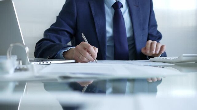 Businessman using calculator and taking notes, working with laptop and documents at office desk. Audit and taxes theme in business