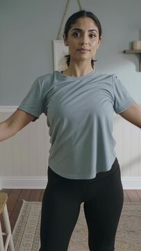 Vertical video: Starting stretch, woman in gym clothes raising arm, bending left at home with rug
