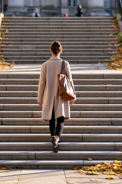 Student walking up wide stone steps on campus with autumn leaves