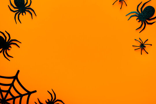 Textured orange background for Halloween, spider web frame and creepy black spiders. Horror theme border. Scary festival decoration concept for autumn celebration poster flyer design