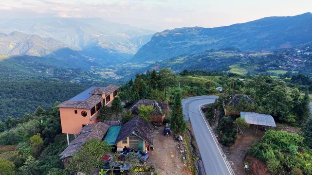 Aerial glide past roadside houses toward misty mountain ranges and terraced villages in Y Ty, Vietnam