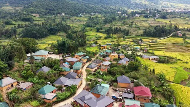 High aerial glide past yellow earthen houses toward distant villages and mountain rice terraces in Y Ty