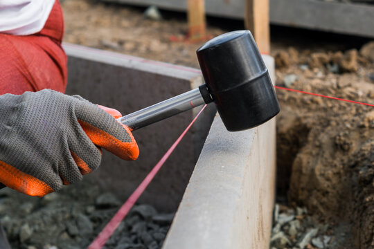 A rubber mallet is used to align a concrete block at a building site, showing the precise work involved in construction.