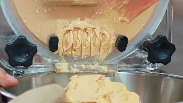 Alternative view of a pink spatula scraping the final batch of fresh Thai tea gelato from a machine.