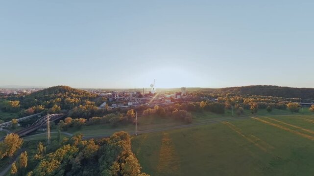 FPV drone reveals the Koksovna coking plant across green fields at sunrise, suitable for industrial development, manufacturing, regional employment and economic activity content.