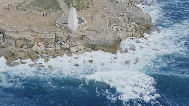 Aerial view of waves breaking against the rocky shoreline beside the Trinity House Obelisk at Portland Bill on the Isle of Portland in Dorset England. The white stone landmark was built in 1844 as a w