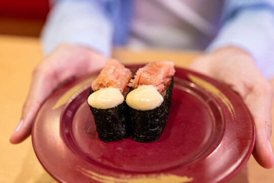 Close-up of woman's hands holding plate with spicy mentaiko mayo gunkan sushi in Japanese restaurant. Delicious gourmet food concept.
