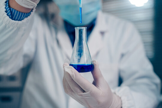 Scientist wearing protective gloves holding two test tubes filled with blue liquid for chemical analysis and scientific research in a laboratory.