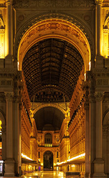Elegant night view inside Galleria Vittorio Emanuele II in Milan, featuring monumental arches, ornate historic architecture, glass-and-iron vaulted roof and warm golden illumination. Iconic Italian sh