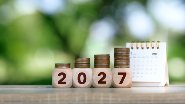 2027 Wooden number blocks and stacks of coins with calendar on green bokeh background for financial planning, savings growth and investment goals. green investment and New Year Resolution concept.