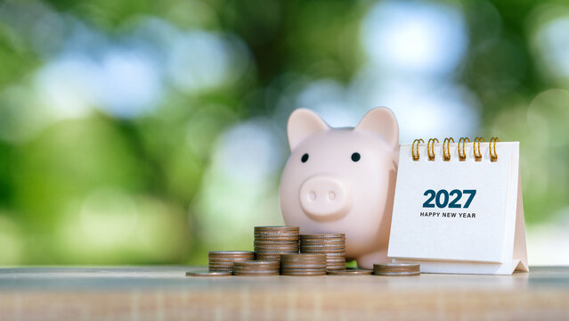 2027 Calendar with stacks of coins and piggy bank on green bokeh background for financial planning, savings growth and investment goals. green investment and New Year Resolution concept.