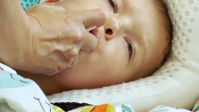 An adult hand sprays medicine into a sick boy's mouth. He lies on a pillow in bed while feeling uncomfortable yet cared for at home.