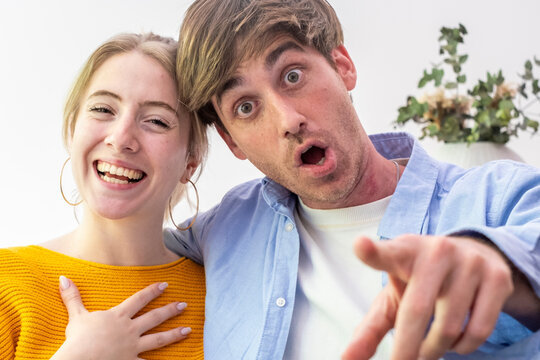 Young couple sharing surprise and joy, woman laughing while man points ahead with wide eyes, candid playful reaction showing connection, excitement and amusement