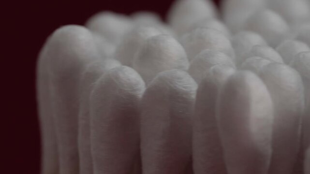 Panning close up of white cotton swabs arranged closely together showing soft rounded tips with fine cotton texture and subtle shadows in detailed view.