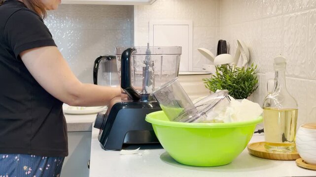 A focused woman prepares a food processor in a bright kitchen. She feels calm and content while making a fresh meal. The peaceful routine brings domestic joy.