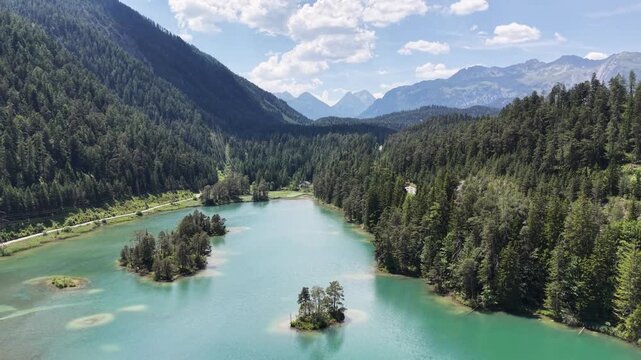 Weissensee turquoise lake dotted with tiny tree islands near Biberwier, Austria, aerial drone pulls back over forest and distant alps peaks.