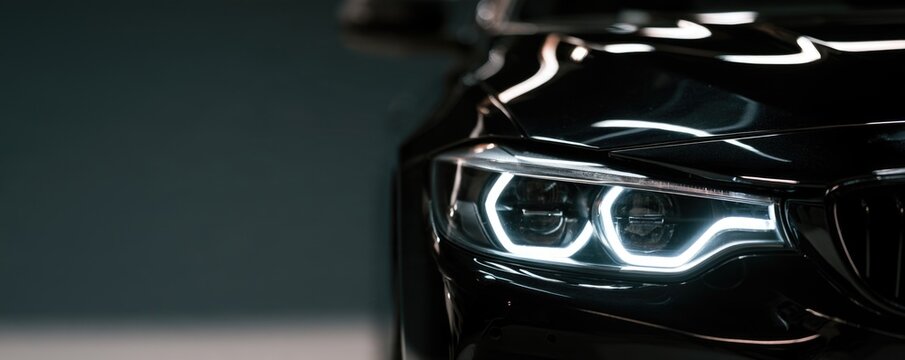 Close-up of a sleek black car's modern LED headlight with reflective surfaces and sharp contours.