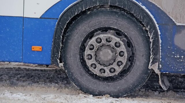 Public bus moves slowly through heavy snowfall as wheels roll across snowy road