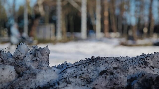 Dirty city snow fills foreground while a mother with baby stroller passes behind