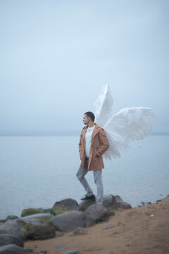 Angel man standing on rocky shore looking at foggy water with copy space