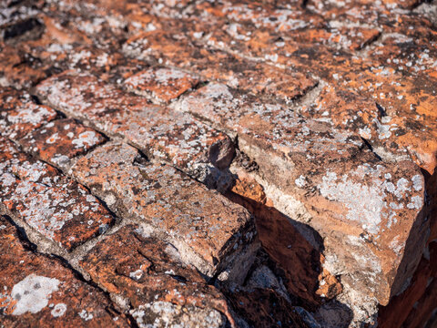 Close-up of an old weathered red brick wall with cracked mortar, worn edges and uneven masonry. Rustic historic brickwork texture showing age, erosion and traditional construction.