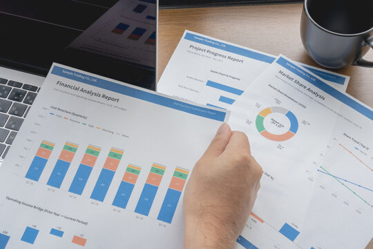 Hand holding a printed financial analysis report with bar charts above project and market share reports.