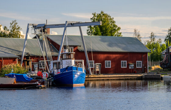 Karlsborg, Sweden - August 18 2026: Traditional blue workboat moored beside historic red boatyard.