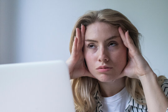 Young woman feeling the burden of work stress, experiencing burnout and mental exhaustion while sitting in front of a laptop, struggling with a headache from excessive work