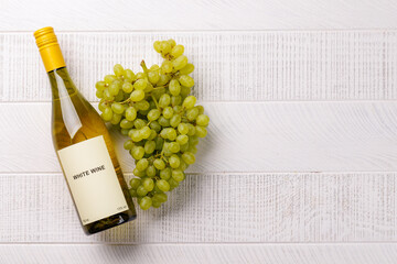 Fototapeta premium White wine bottle and green grapes on white wood