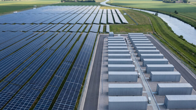 Aerial view of solar farm with battery energy storage system, photovoltaic power plant and BESS container near river for renewable electricity and grid stability